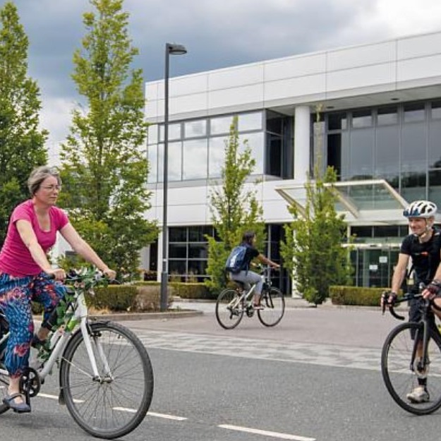 Picture of three people cycling infront of an office building