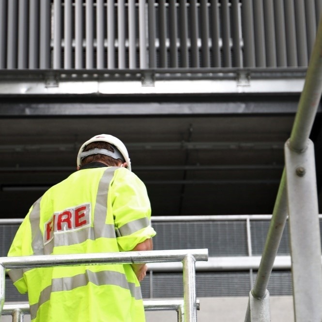 Picture of man wearing a high vis fire vest and white helmet on scaffolding outside building.