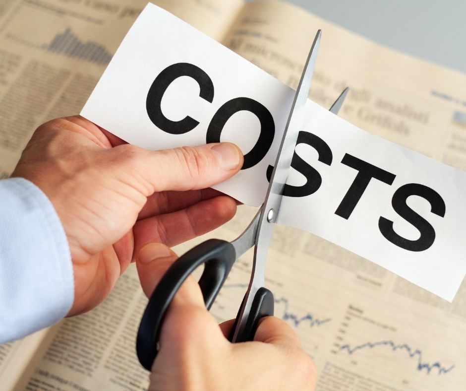Hands cutting a paper labeled “COSTS” with scissors over a newspaper background.