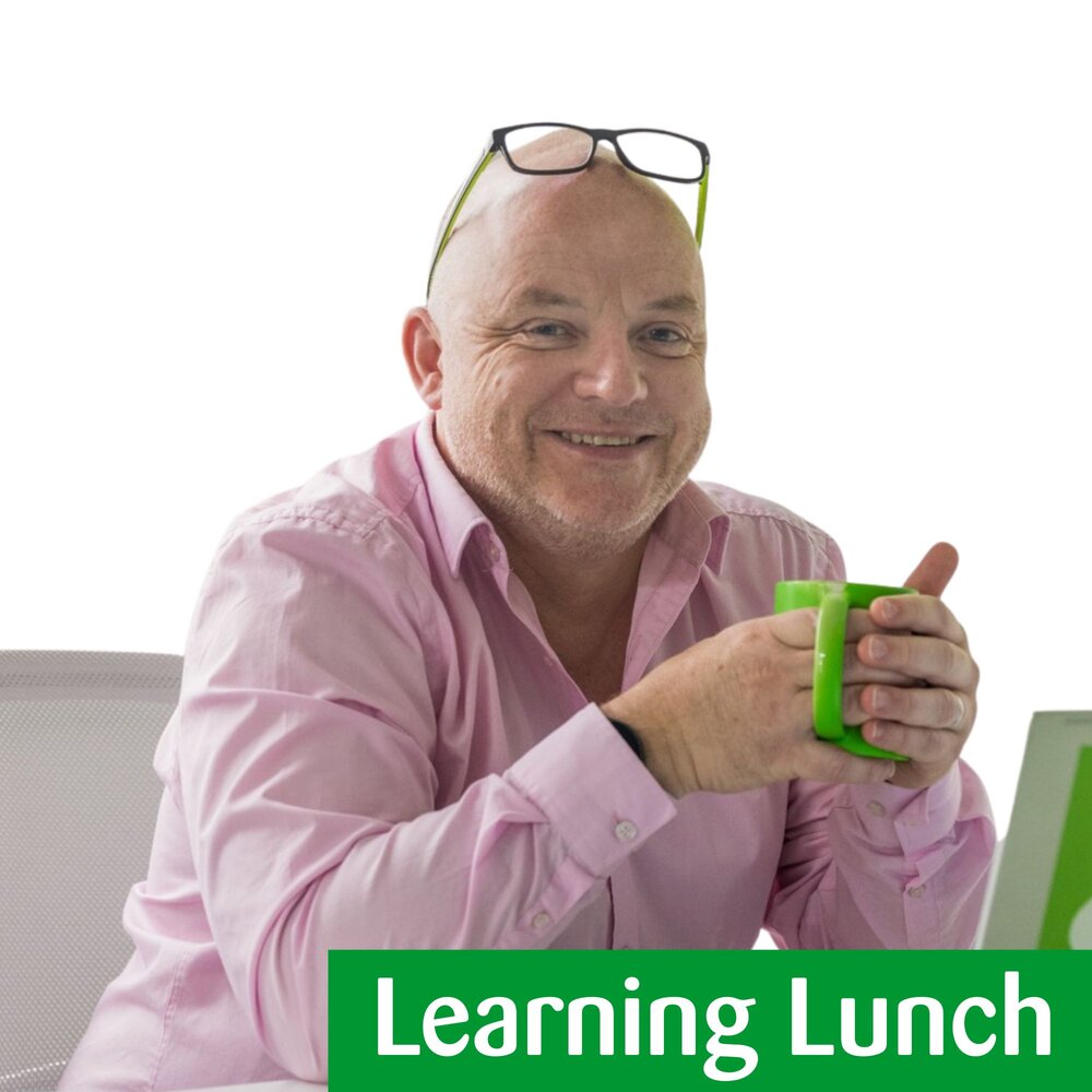 Photo of man in pink shirt, smiling with glasses on his head. he is holding a green mug.