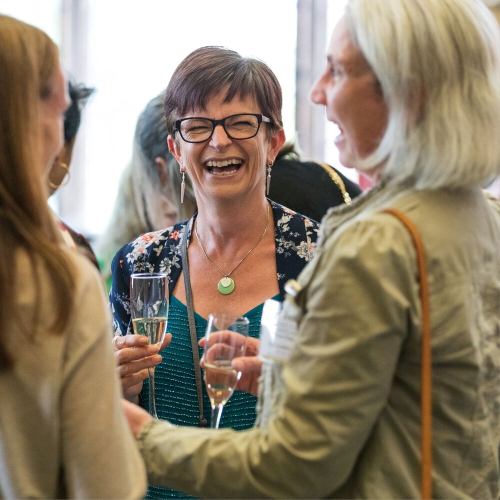 Lady with glasses and short hair smiling holding a champagne flute.