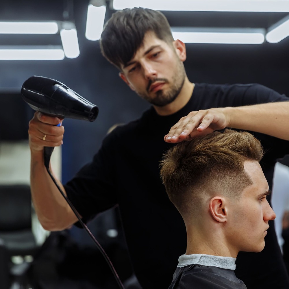 Photo of a male hairdresser with beard blow drying a customers hair