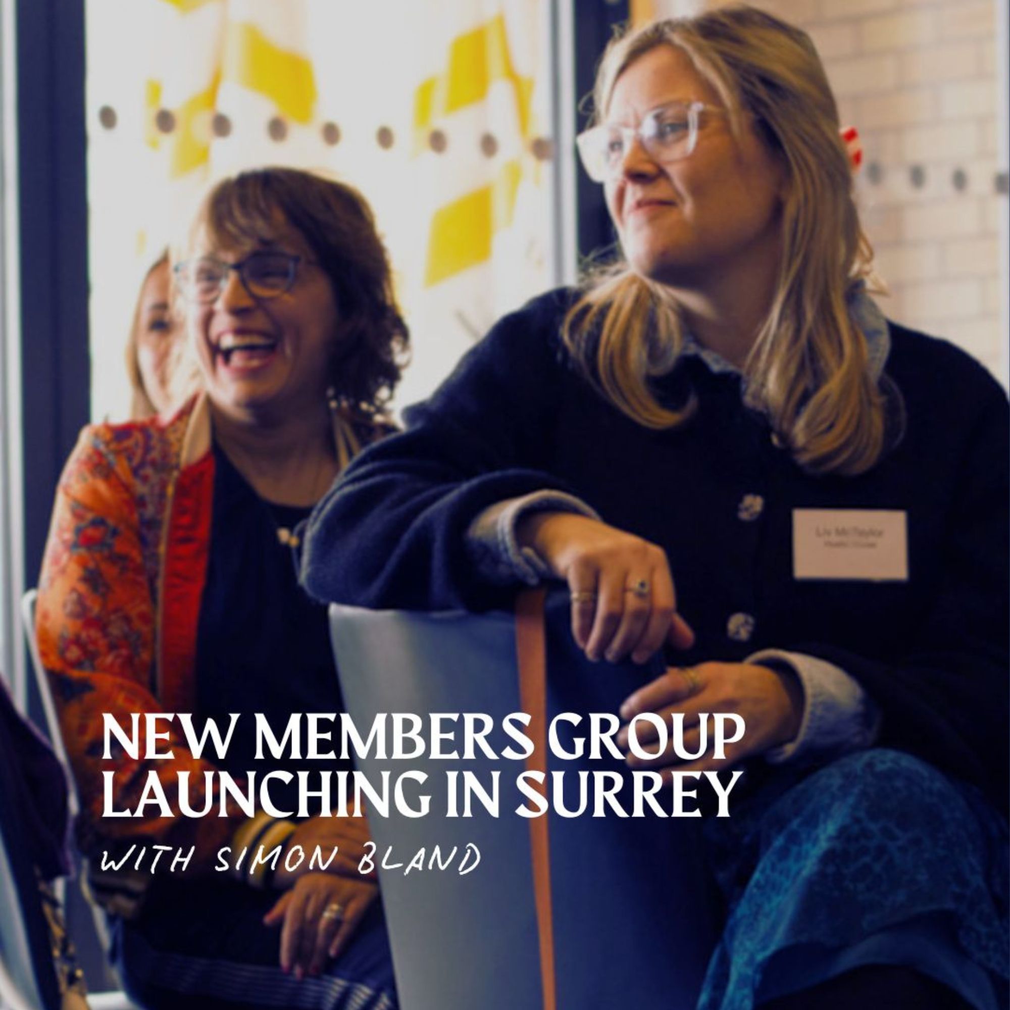 People seated and networking at a business event. In the foreground, a person wearing glasses sits on a chair facing to the side, while another attendee is seated nearby. The image features the promotional text: “NEW MEMBERS GROUP LAUNCHING IN SURREY” and “WITH SIMON BLAND”. The setting appears to be an informal professional gathering.