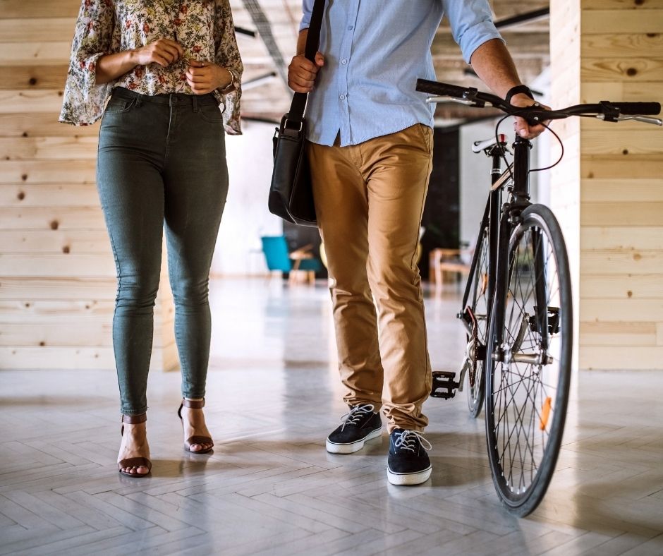 Two people walking indoors, one holding a bicycle and a shoulder bag, in a modern wooden-paneled space.