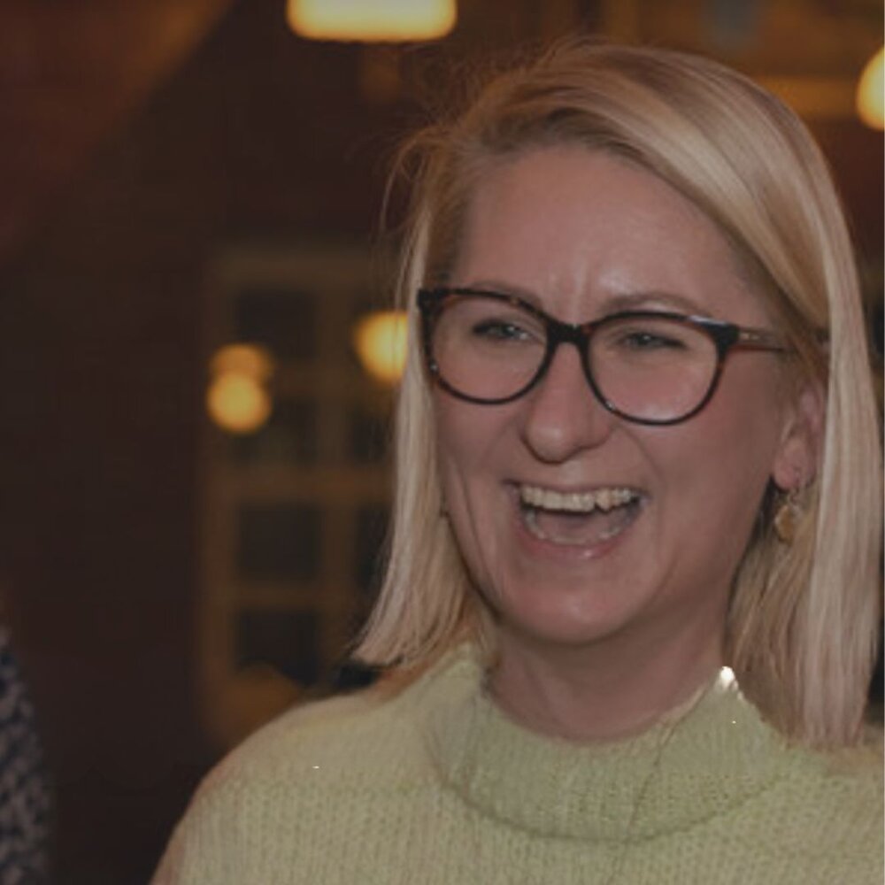 Blonde lady with glasses smiling at evening networking event