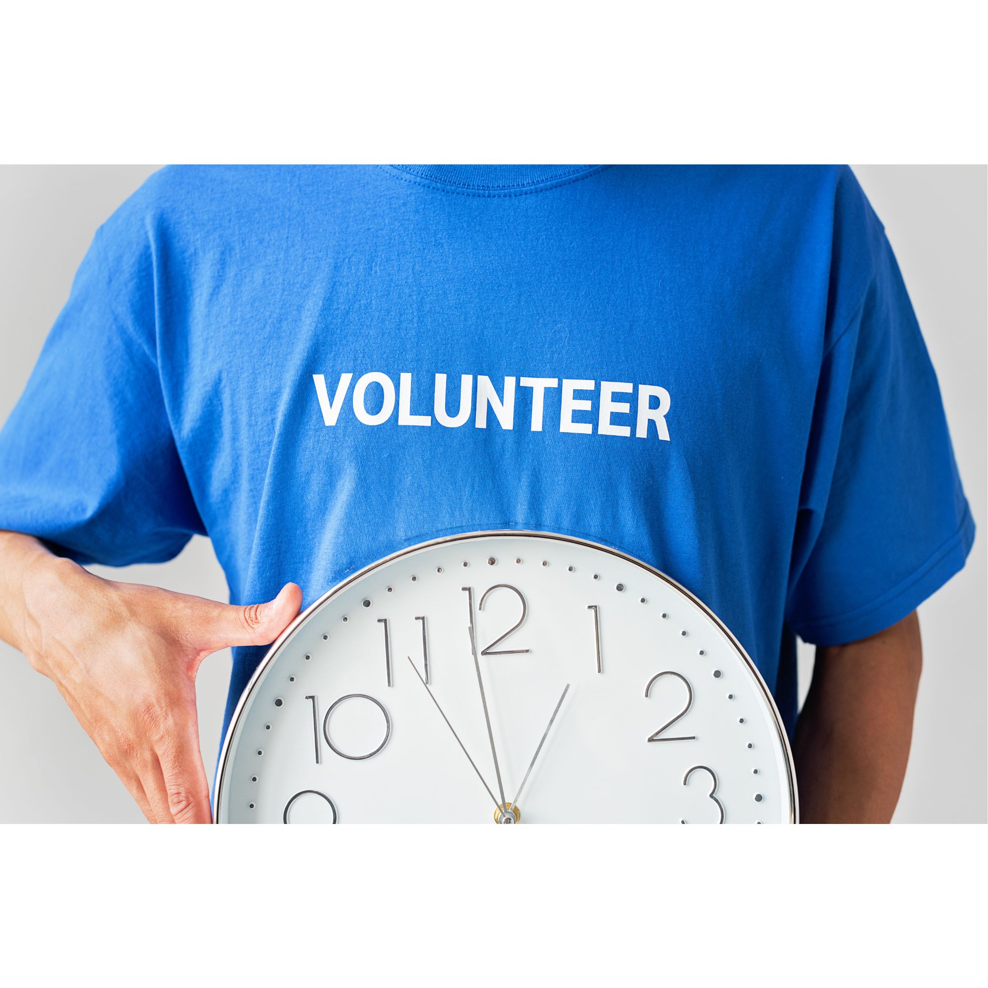 Person wearing a blue T-shirt with the word “VOLUNTEER” printed in white, holding a large wall clock against their torso.