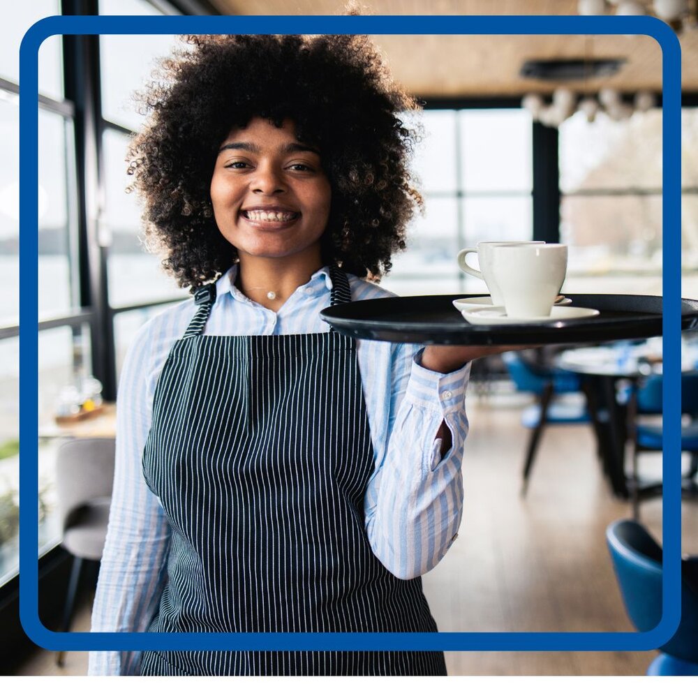 Waitress with blue apron and blouse holding a tray at her shoulder with a coffee cup