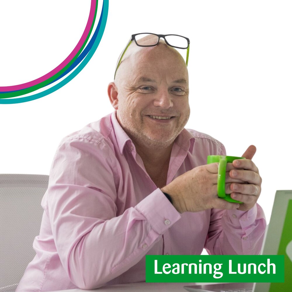 Photo of man in pink shirt, smiling with glasses on his head. he is holding a green mug.