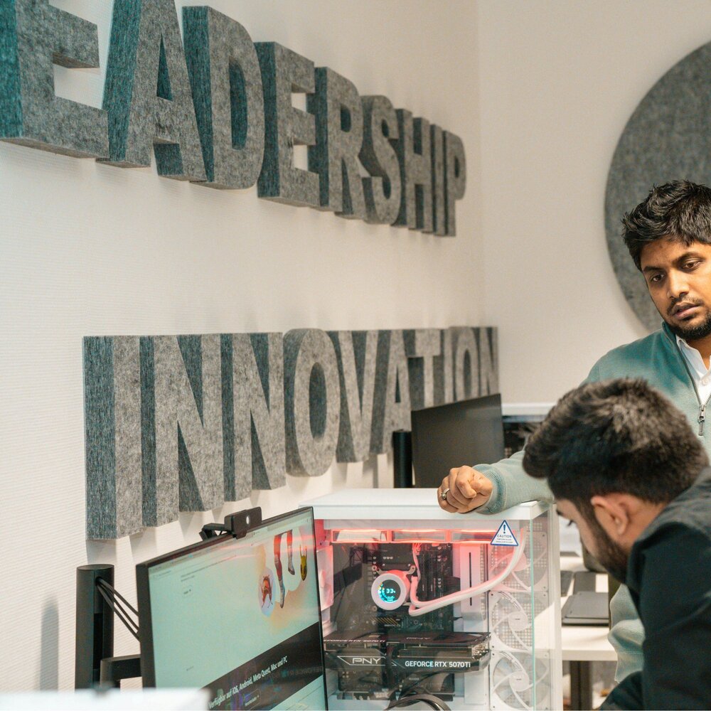Three people gather around a computer, with "Leadership" and "Innovation" in grey block letters on the wall.