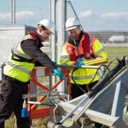 Two men in hard hats and high visibility jackets with a mechanical digger at Gatwick AIrport