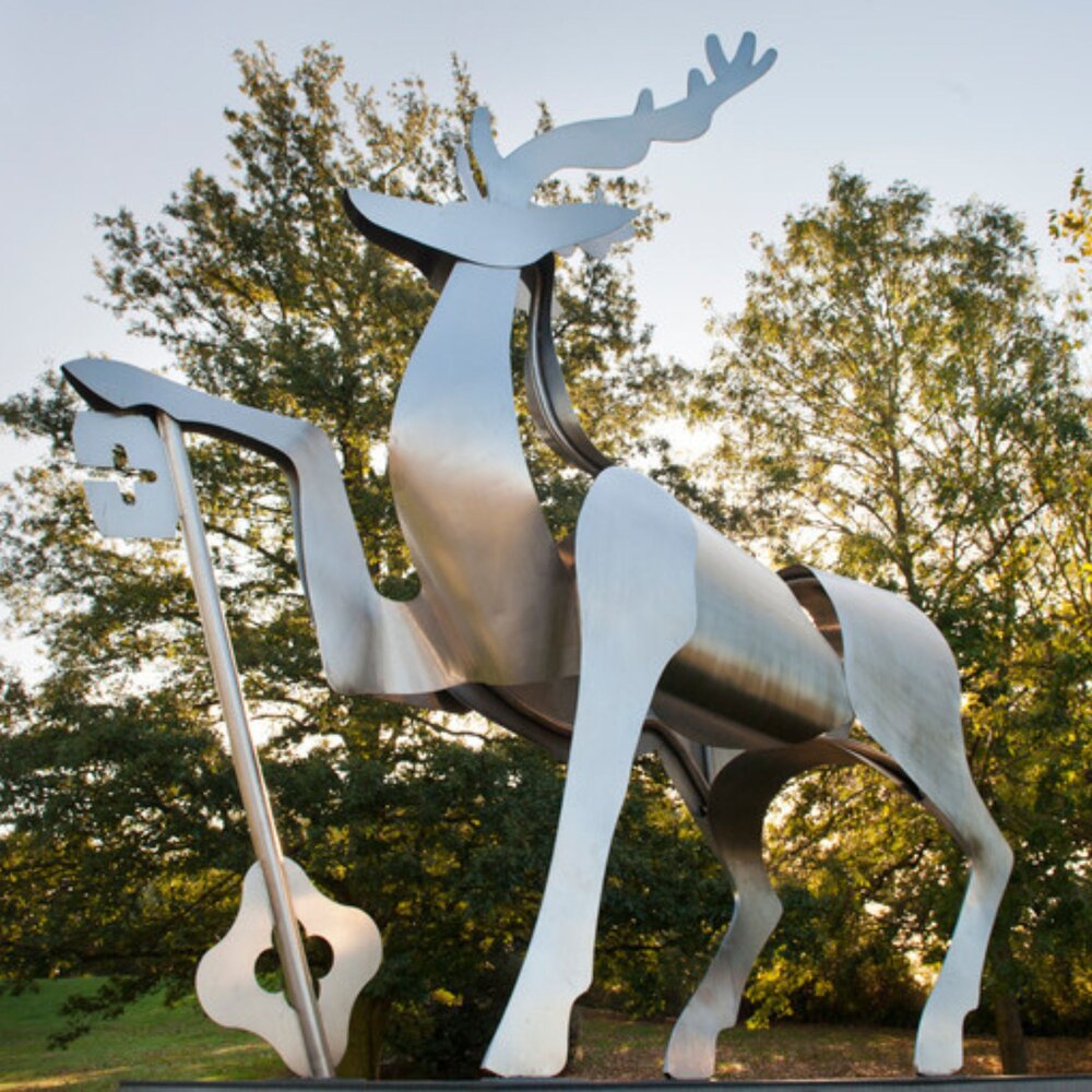A metal sculpture of a deer holding a key, set against a backdrop of trees.