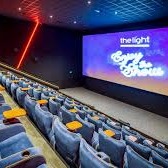 Photo of the insice of the cinema, blue tiered velvet seats red light and text on screen.