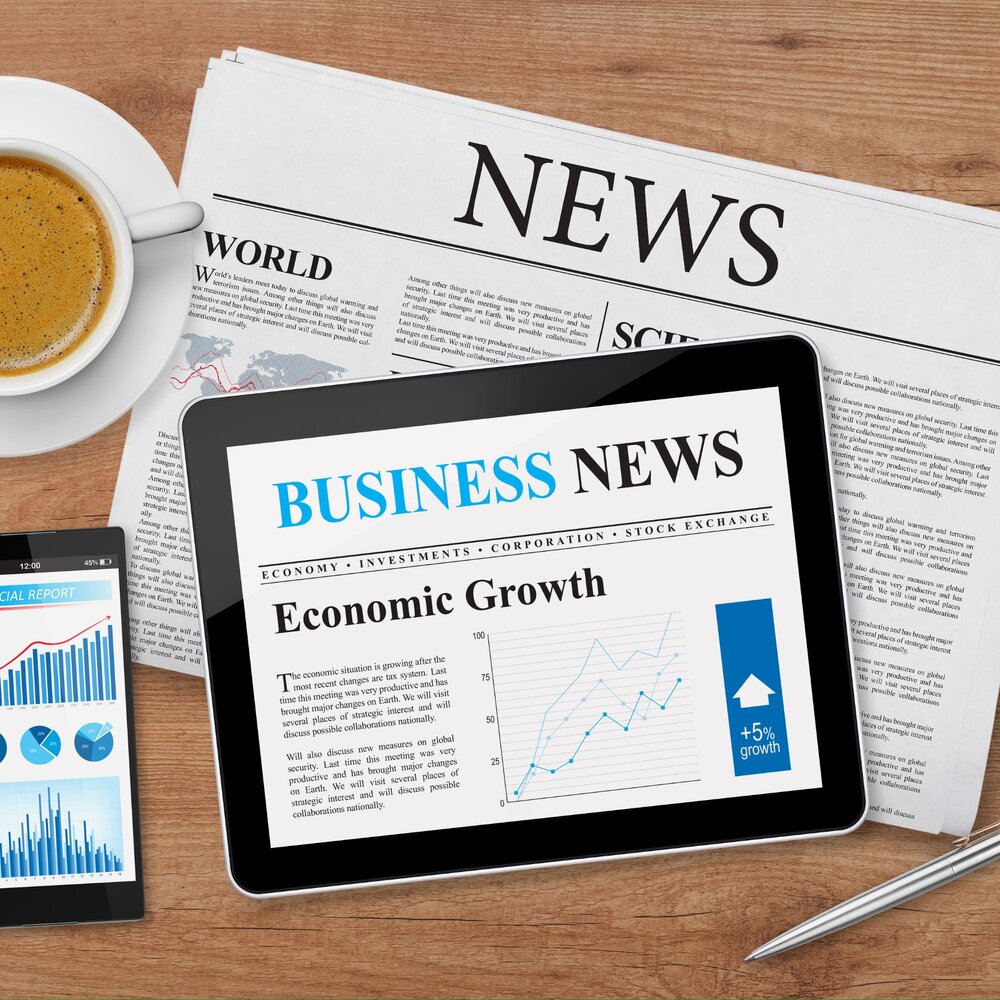 Image of a computer tablet, newspaper, mobile phone and cup of coffee on a desk. Tablet reads - business news