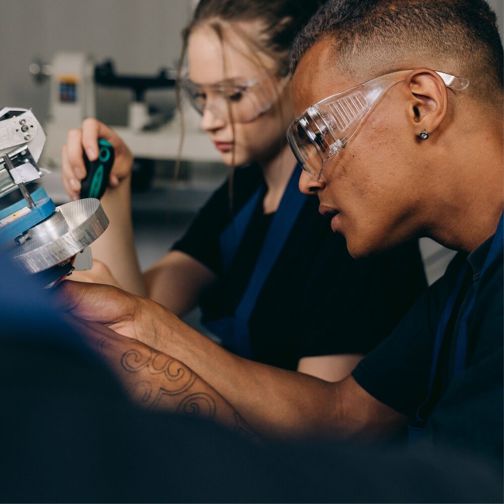 Man and woman working on machinery wearing protective goggles